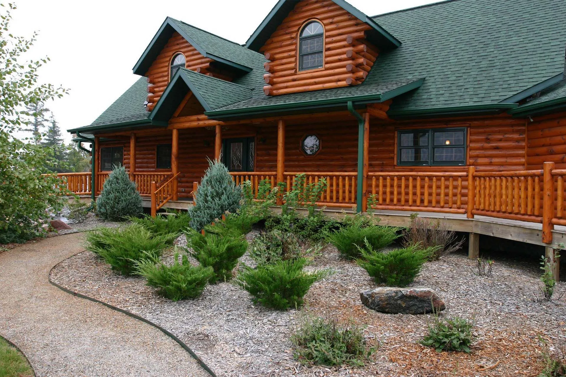 An image of a log house, a backyard with several plants and a walkway