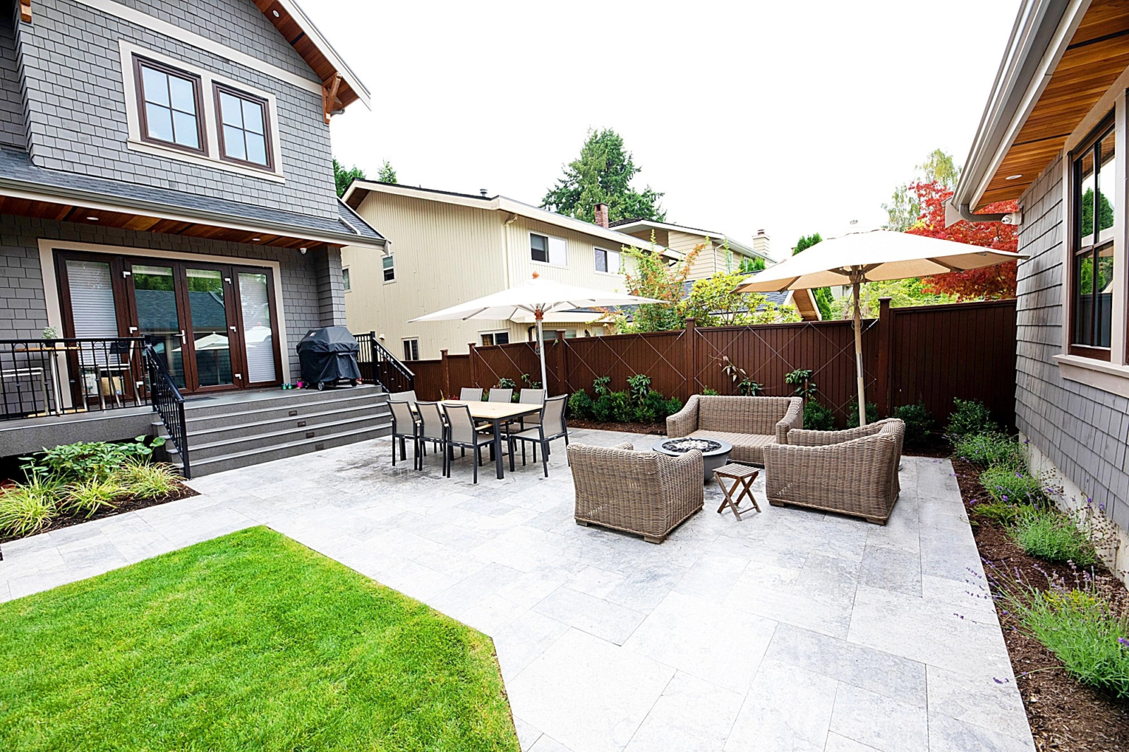 A picture of a backyard deck with numerous tables and chairs as well as lounge umbrellas.