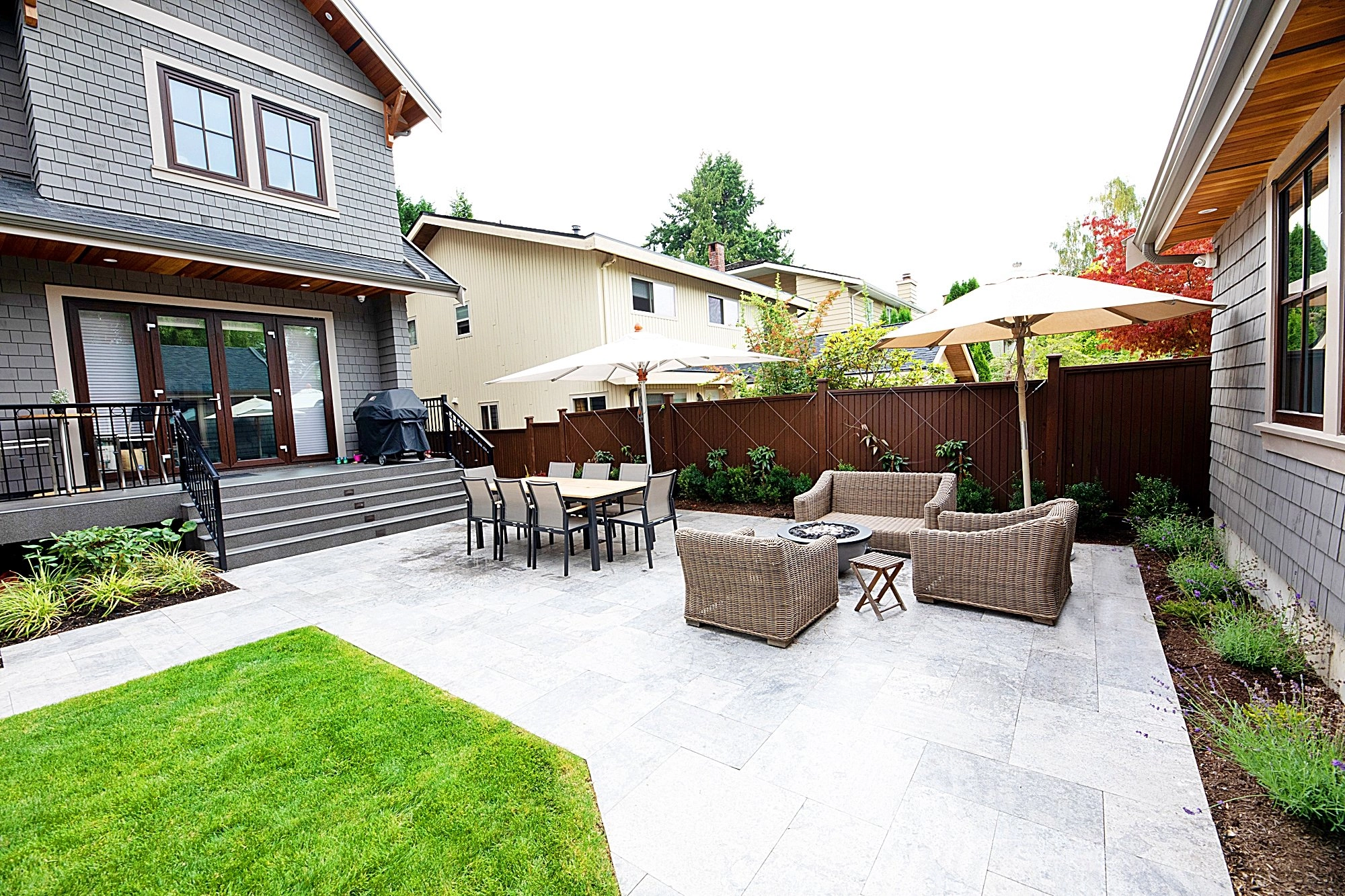 A picture of a backyard deck with numerous tables and chairs as well as lounge umbrellas.