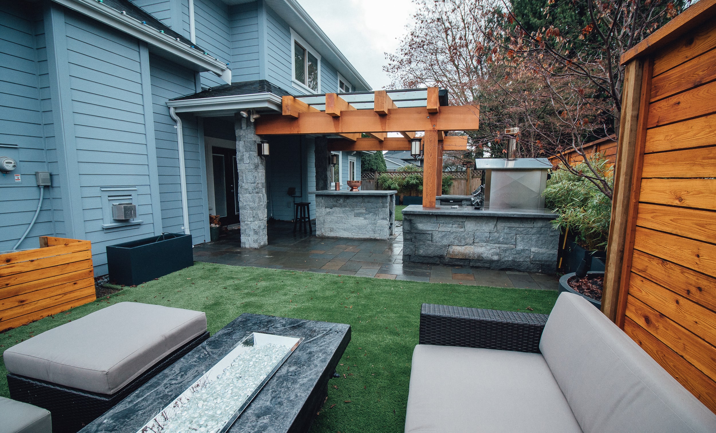 A backyard garden landscape with outdoor furniture and a grill in the background.